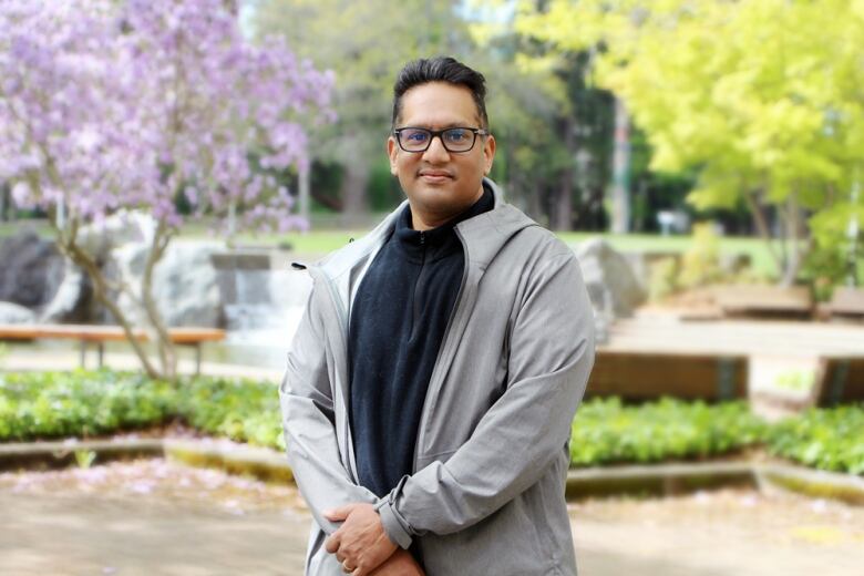 A man wearing glasses stands in a park.