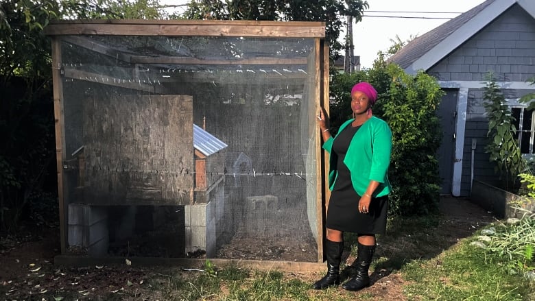 Woman in green blazer and purple headscarf is standing beside a large chicken coop. 