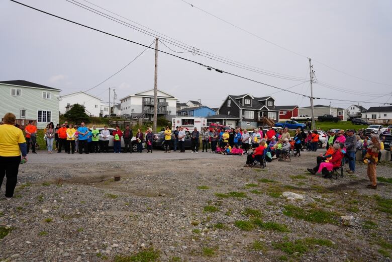 A large crowd of people stand in a semi circle. Many of them are wearing coloured t-shirts, which feature a logo of a tree with the text 'Stronger than the storm' underneath.