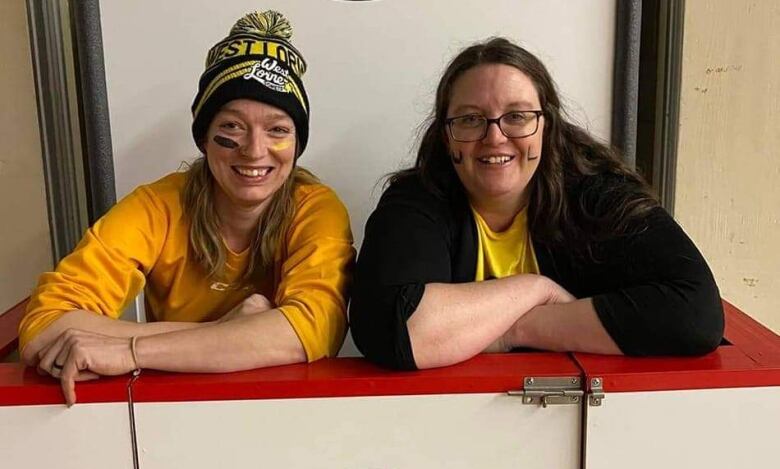 two women, one in yellow the other in black, in front of West Lorne Comets sign.