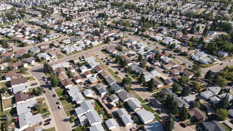 An aerial view of houses in a neighbourhood during the day, with trees and green lawns.