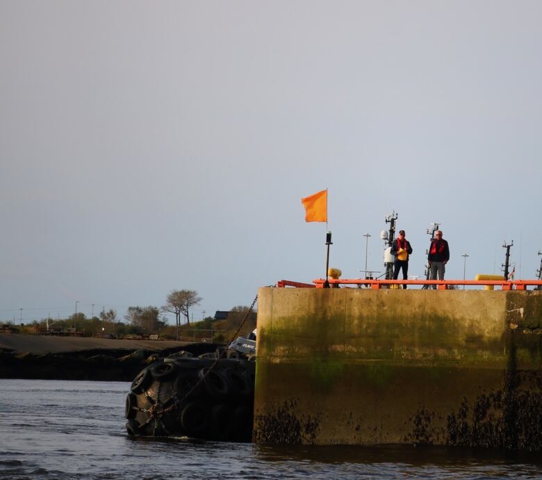 Two sailboat race officials stand by an orange flag that marks the starting line of the Digby Race. 