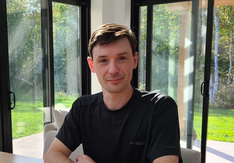 A man with short brown hair sits indoors looking at the camera.