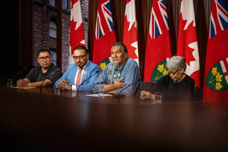 A group of people sit at a desk and take questions from reporters. 