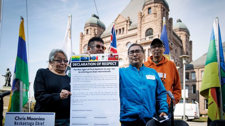 A group of people stand outside, holding a large sheet of paper.