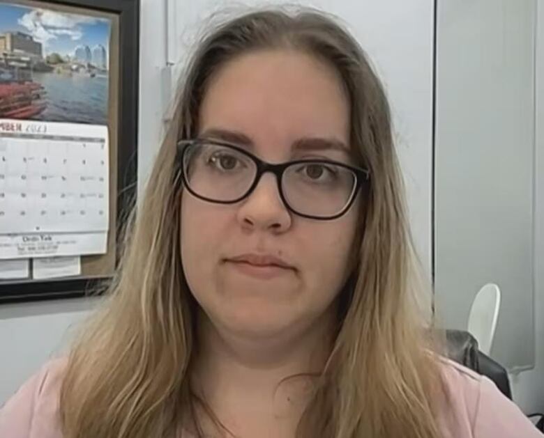 A woman with long light hair and glasses sits in an office.