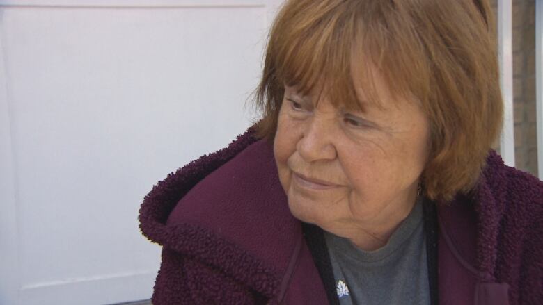 A woman wearing a purple hoodie sits in front of a white door.