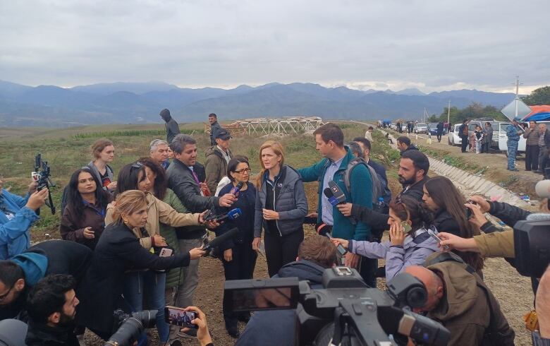 A woman stands in a field surrounded by reporters