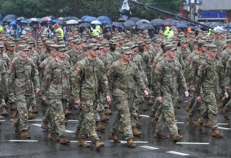 Dozens of unarmed soldiers in military fatigues are shown walking.