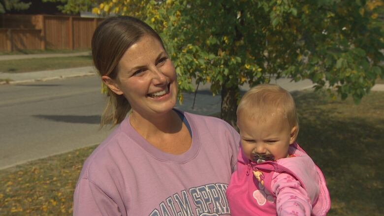 Woman with light brown hair wearing a light purple sweatshirt holds her infant daughter.  