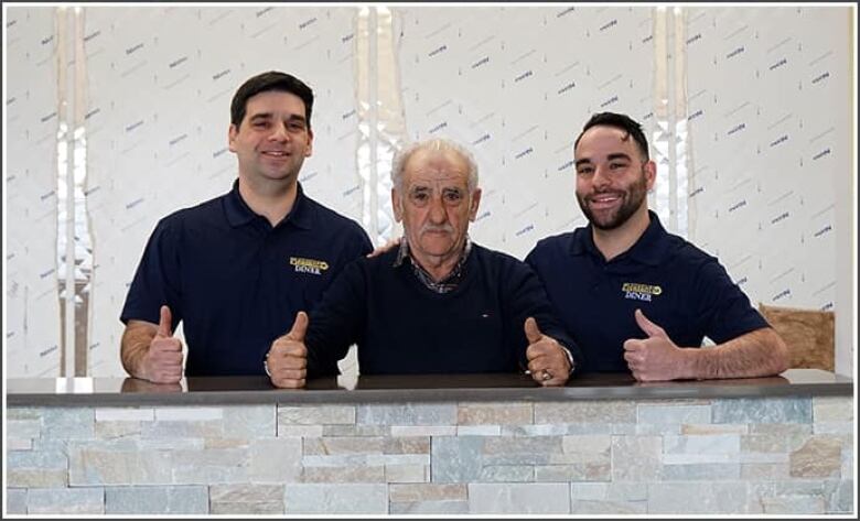 Three men in black polos pose for a photo and give a thumbs up.