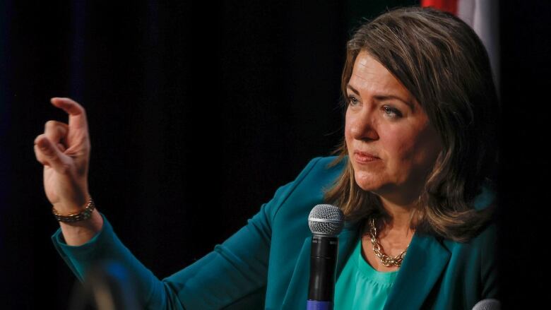 A woman in a green blazer makes a gesture.