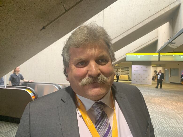 A man in a suit stands in a conference centre.