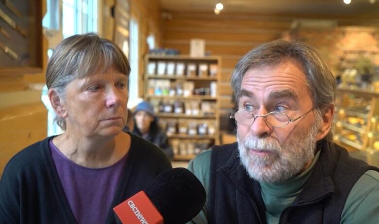 A man and a woman sit inside an eatery, in front of a CBC microphone.