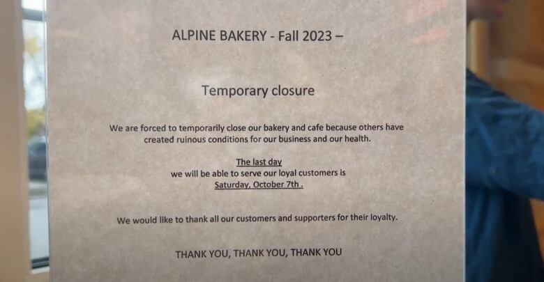 A printed sign stuck on a glass door announces the temporary closure of the Alpine Bakery.