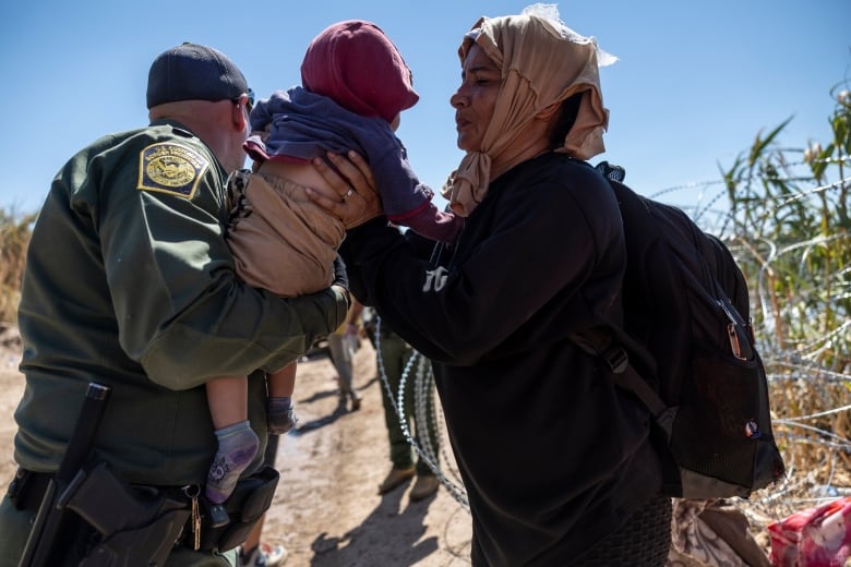 A very small child is passed between a woman and a man in uniform.