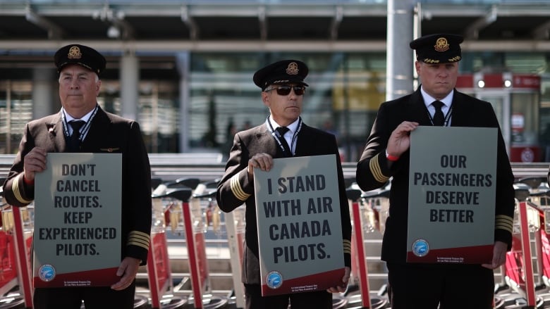 Pilots stand outside of Toronto Pearson airport holding signs that read 