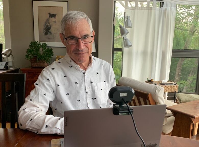 Man sits behind a laptop at his dining room table.