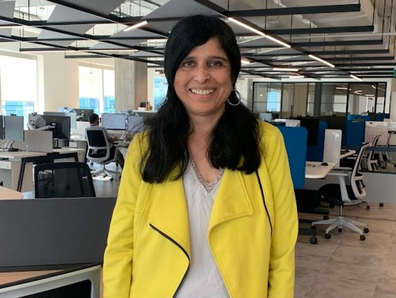 A woman stands in an office with rows of desks behind her