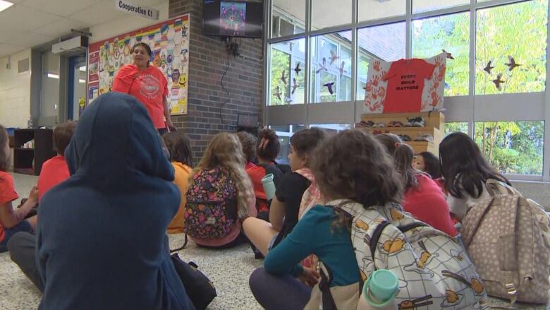 A teacher talks to students sitting on the ground. 