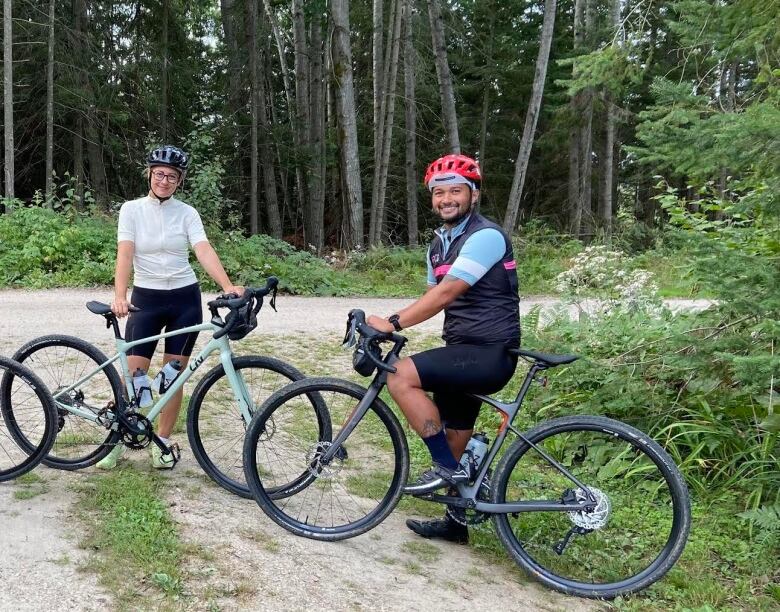 A woman and a man stand smiling holding their bikes. 