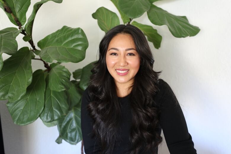 A young woman in a black shirt in front of a big green plant. 