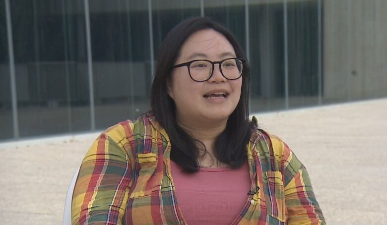 A young woman in a plaid shirt talks to the camera.