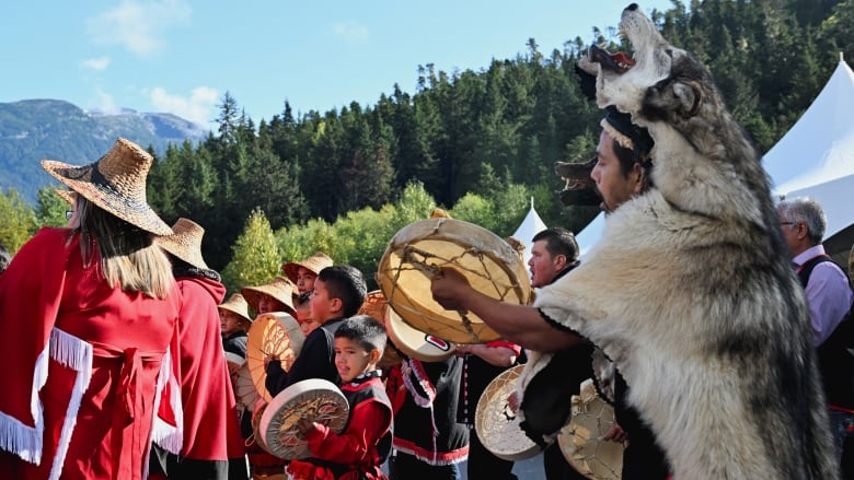 People are pictured in traditional clothing singing and playing drums.