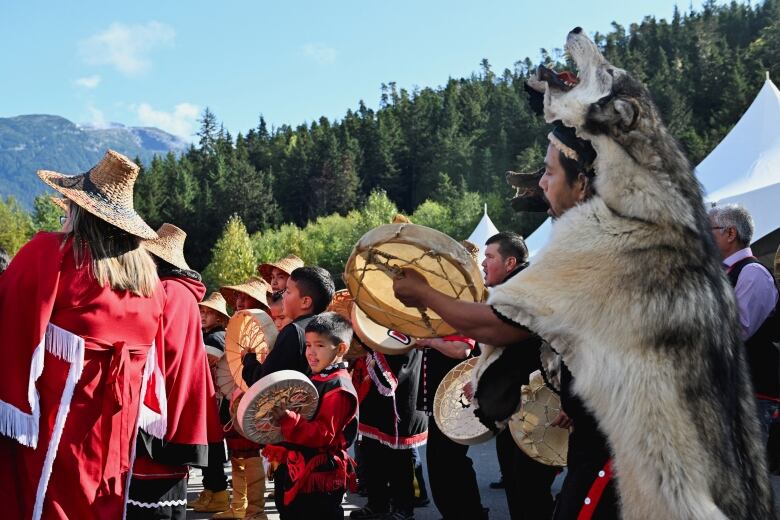 People are pictured in traditional clothing singing and playing drums.