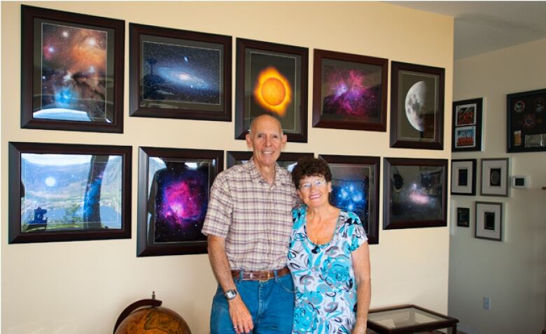 A man and a woman stand in front of a wall of images of space. 