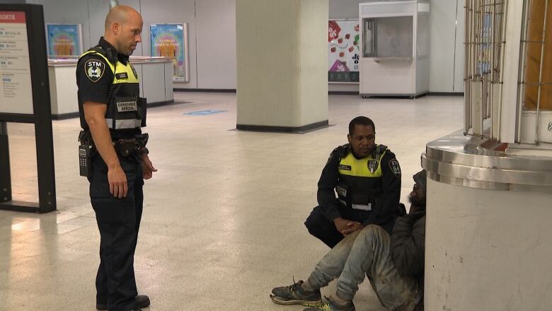 Two men stand close to a man on the floor.