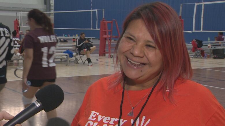 Sheila Grandbois smiles during an interview in front of a volleyball court.