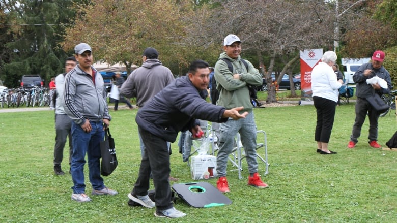 One man throwing a small bag, while two other watch him.