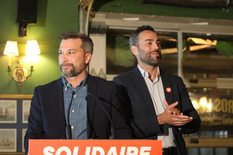 Two men at an orange podium.