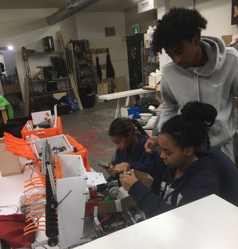 Three high school students work on a machine with bright orange tubes.