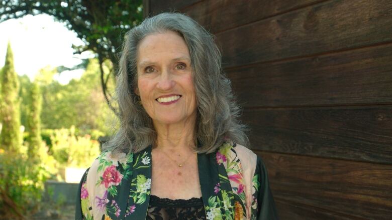 A gray-haired woman wearing a floral shirt smiles.