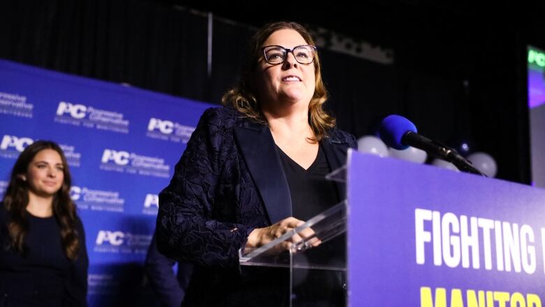 A woman is shown speaking at a podium.