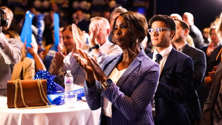 A Black woman claps while watching a speech. 