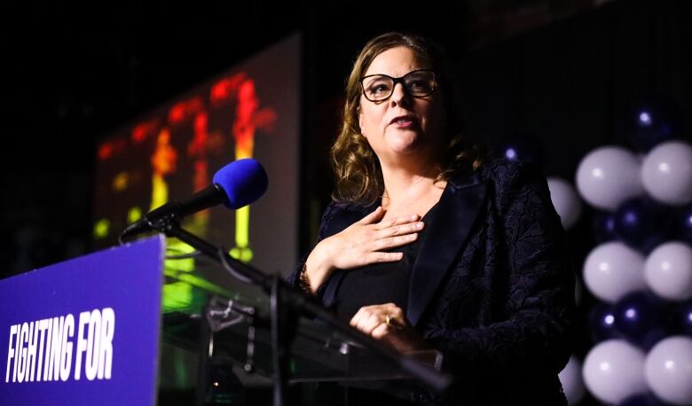 A woman is shown speaking at a podium.