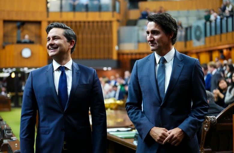 Two politicians smile and look to their right in a legislature as they stand and wait for something.