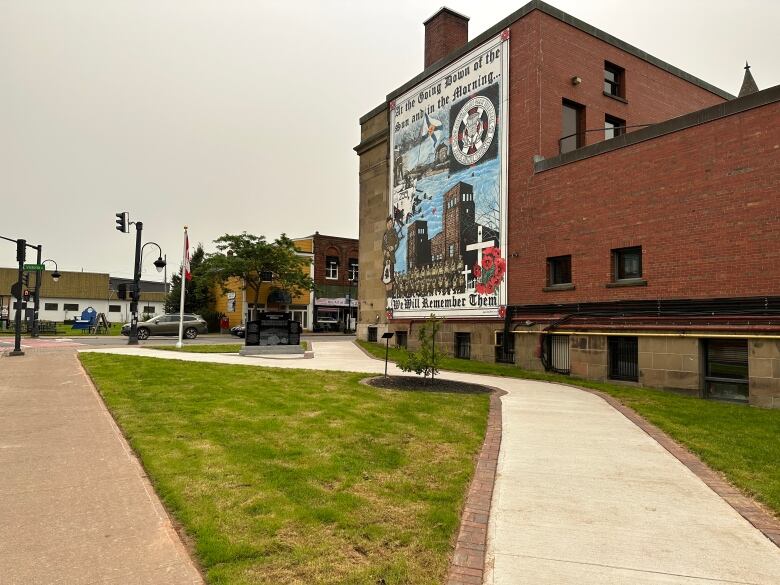 A concrete pathway is shown leading to a large military mural at Amherst town hall. A black stone Afghanistan war memorial is in the centre.