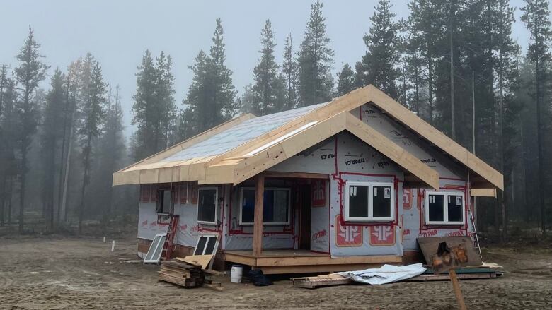 A timber home under construction in a misty forest. 