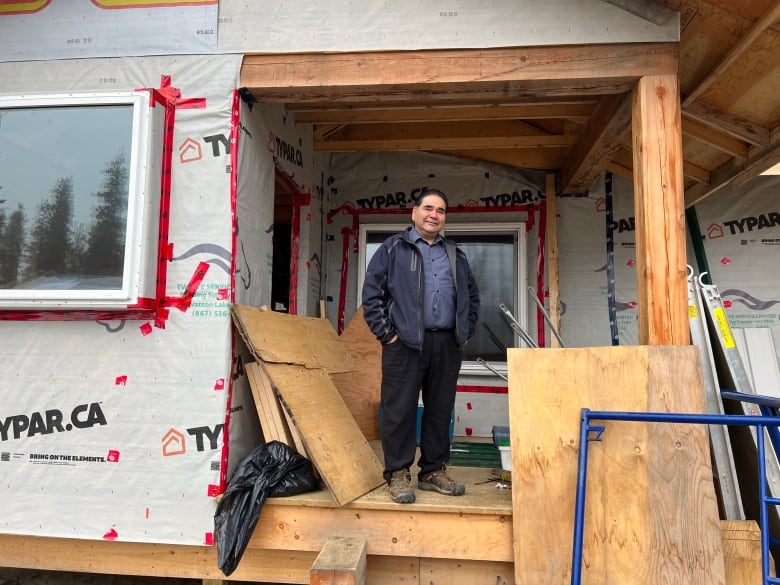 A man stands on the porch of an under-construction home. 