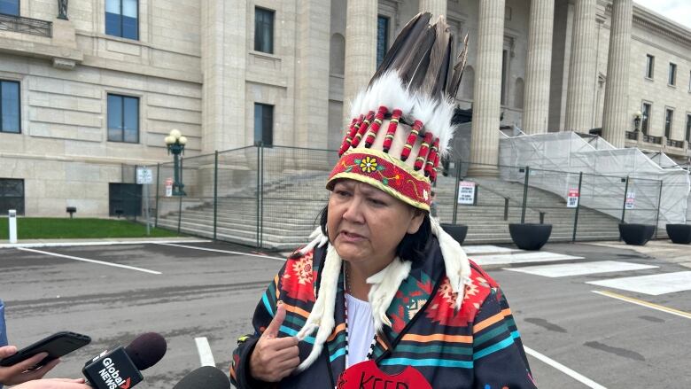 A woman in Indigenous regalia speaks to media. 