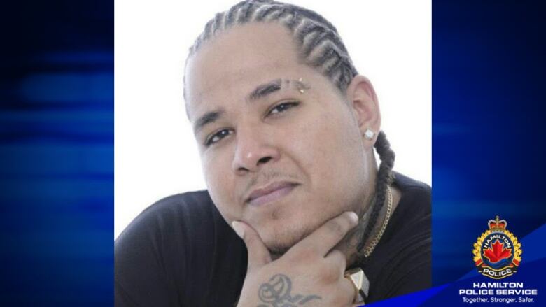 A portrait of a man with cornrows posing with his hand on his chin. There is a Hamilton police Service watermark on the image. 