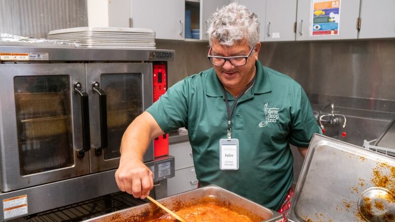 A man stirs a large tray of pasta sauce.