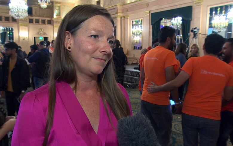 A woman wearing a pink top speaks to a reporter off camera. 