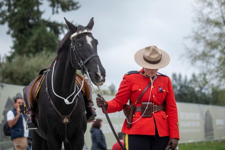 A Mountie in red serge leads a riderless horse.