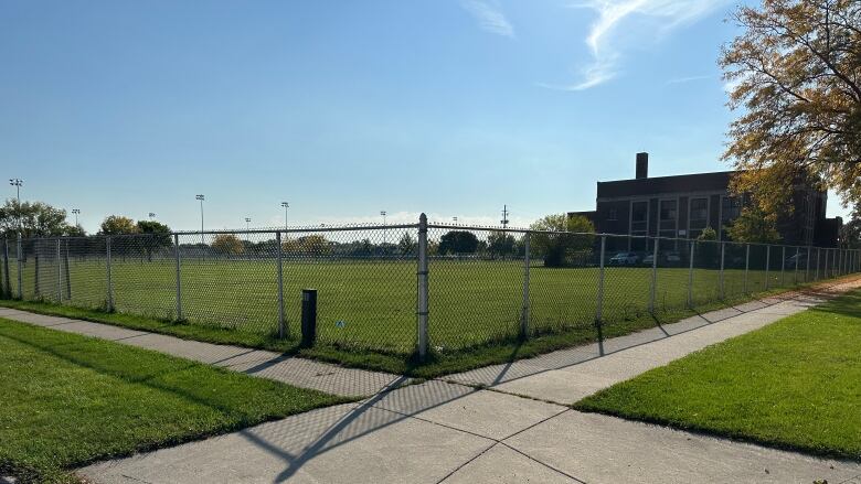 A grassy vacant lot in front of a historic school building.