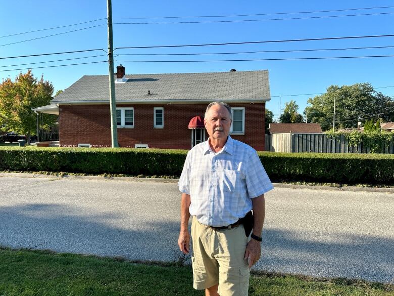 A man stands in front of his one-storey home.